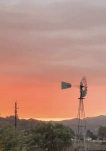 Sunset with a windmill, trees, and mountains.